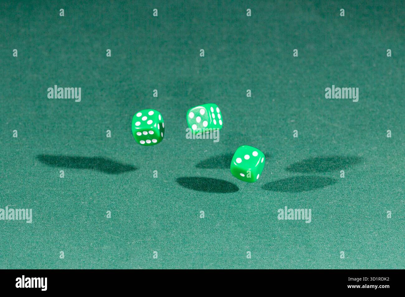Three green dices falling on a green table Stock Photo
