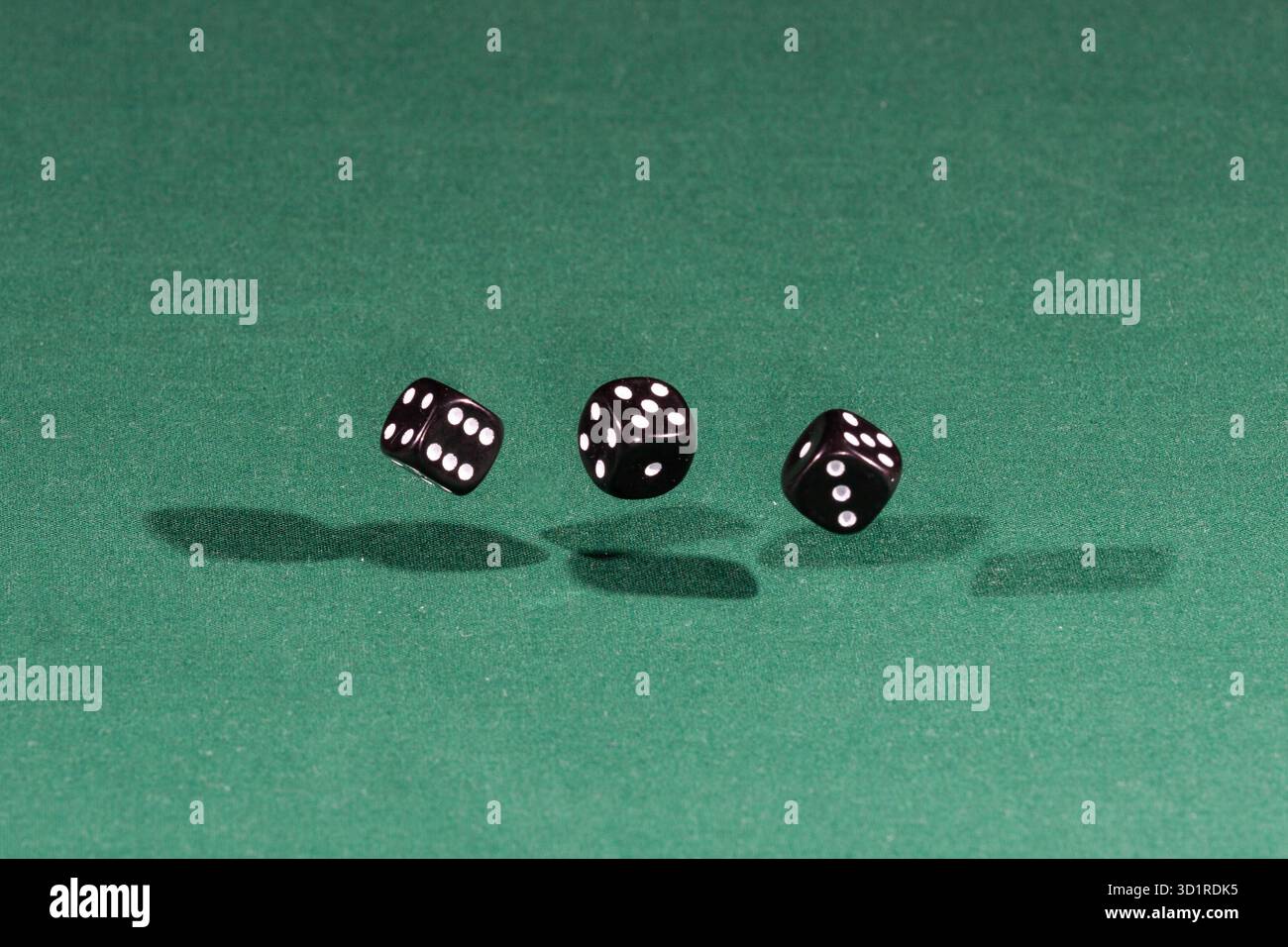Three black dices falling on a green table Stock Photo