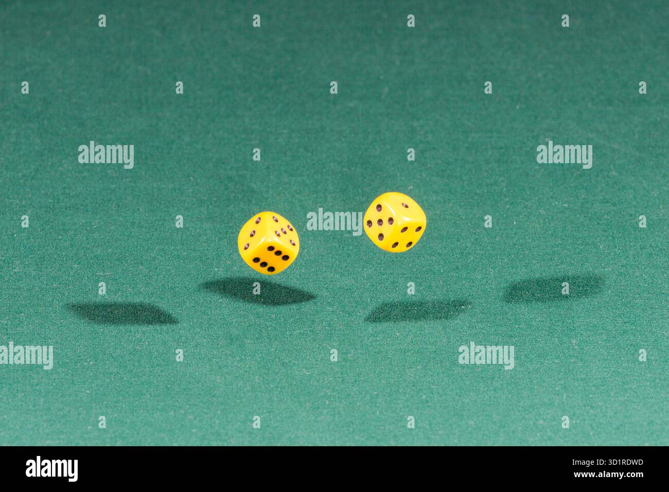 Two yellow dices falling on a green table Stock Photo