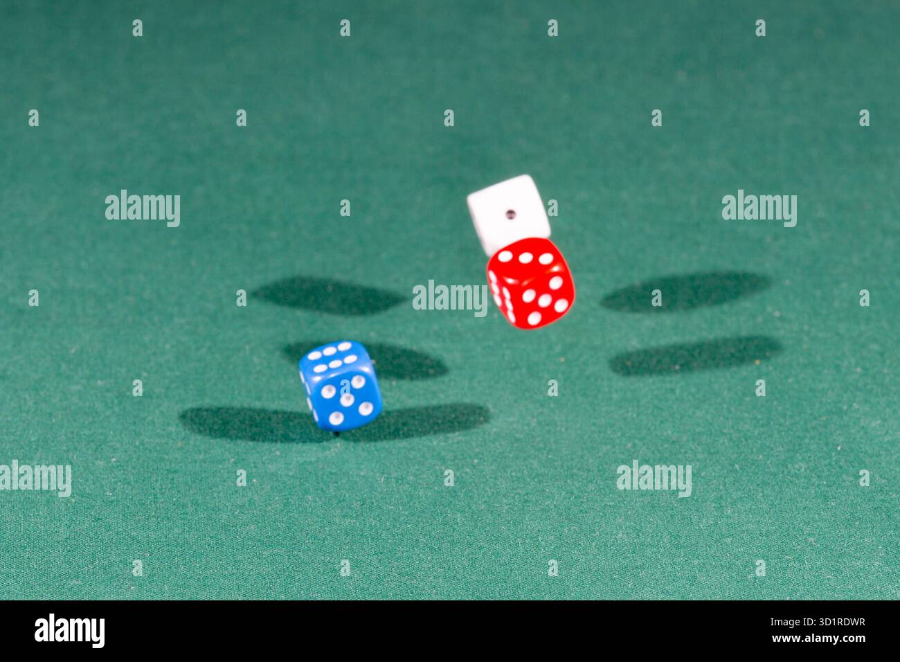 White, red and blue dices falling on a green table Stock Photo