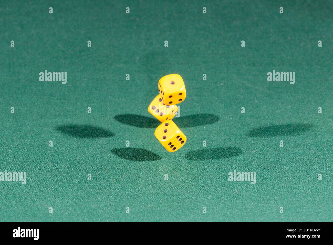 Three yellow dices falling on a green table Stock Photo