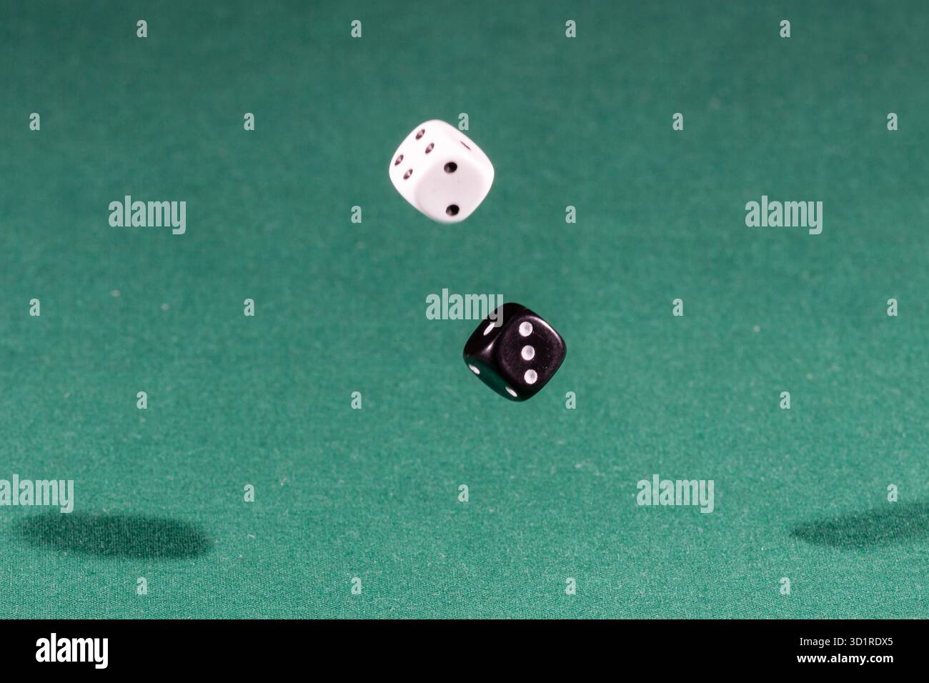 Two white and black dices falling on a green table Stock Photo