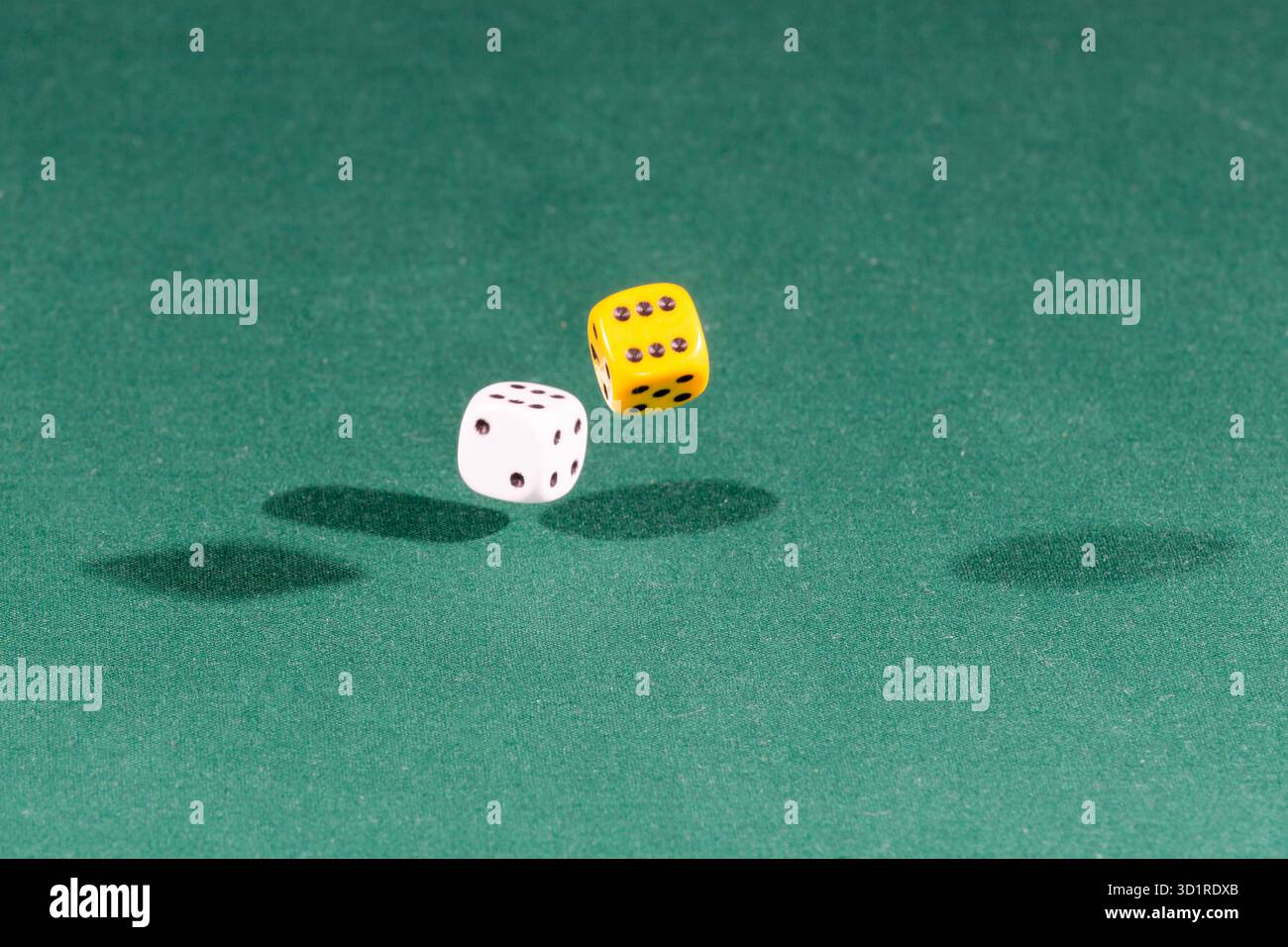Two white and yellow dices falling on a green table Stock Photo