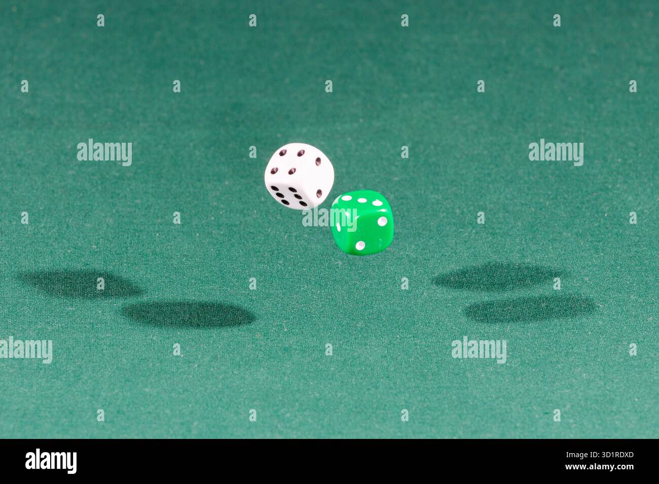 Two white and green dices falling on a green table Stock Photo