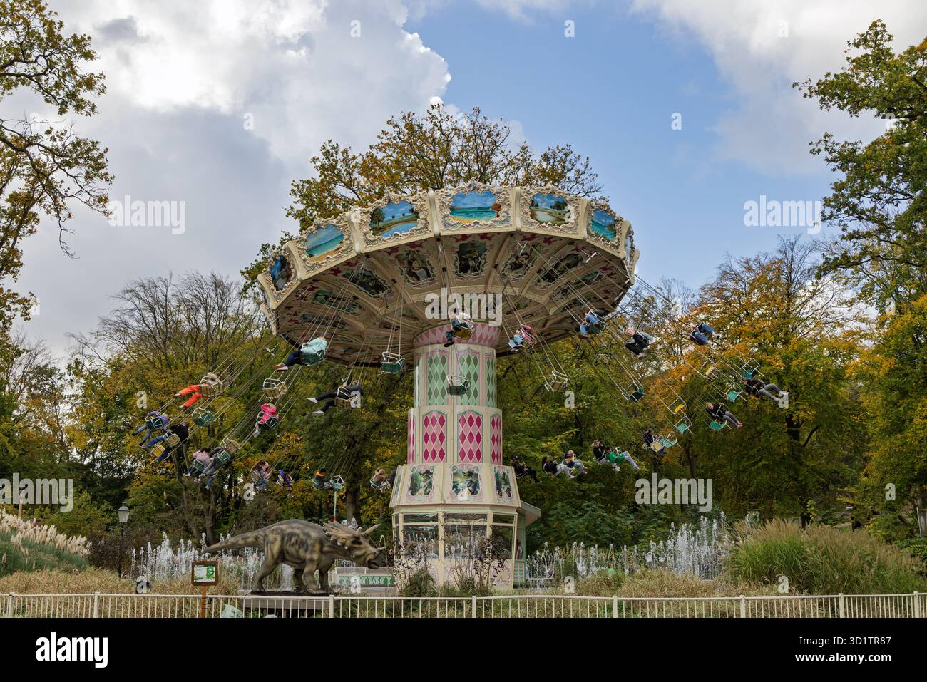 The Aqua Swing carousel at Duinrell, a classic swing ride with colorful jungle and dinosaur motifs, spins high above the park's landscaped grounds. Wa Stock Photo