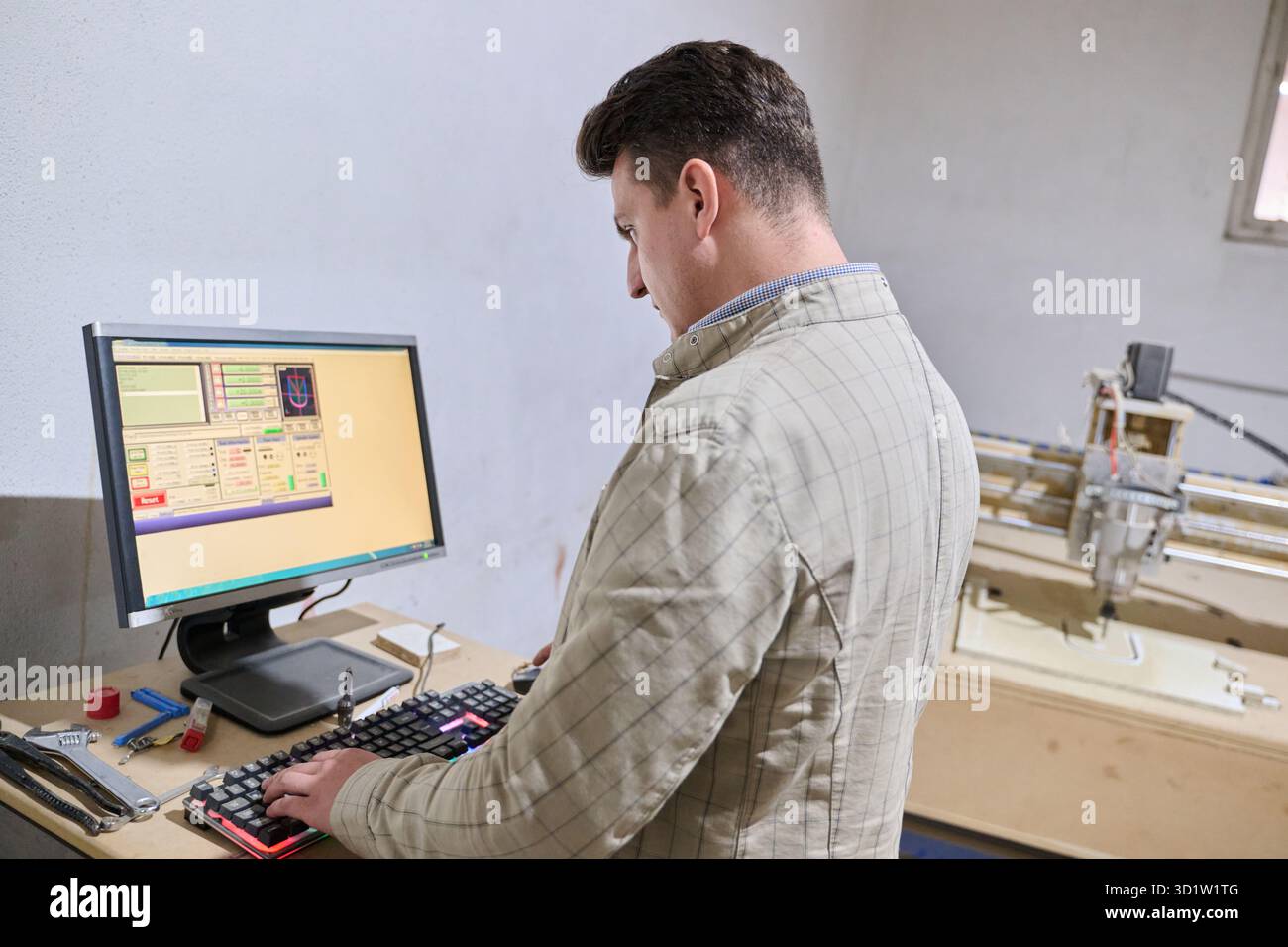 Operator Entering Coordinates on Computer for CNC Machine to Precisely Cut Wooden Pieces Stock Photo