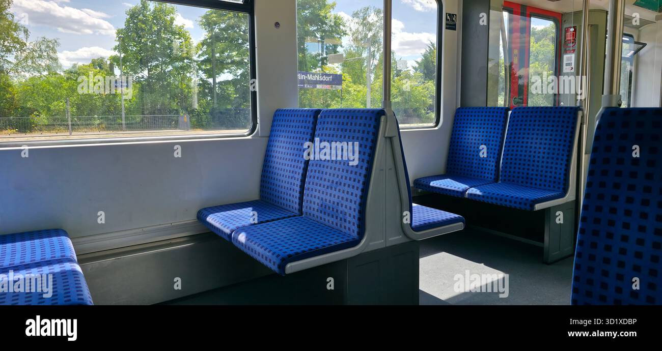 Berlin, Germany - July 04, 2025: Interior view of an empty train carriage featuring blue patterned seats and large windows with greenery outside. - Smartphone Captured Stock Image
