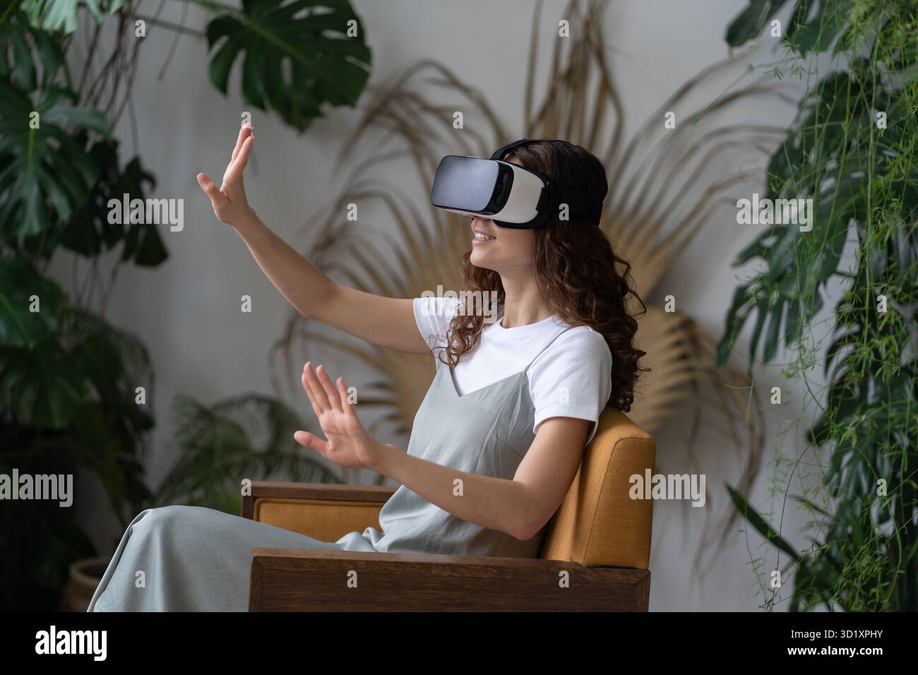 Young woman wearing VR helmet experiencing virtual reality while resting in greenhouse Stock Photo
