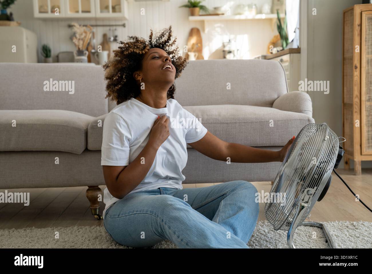 Young African American woman cooling down by ventilator at home, feeling unwell during heatwave Stock Photo