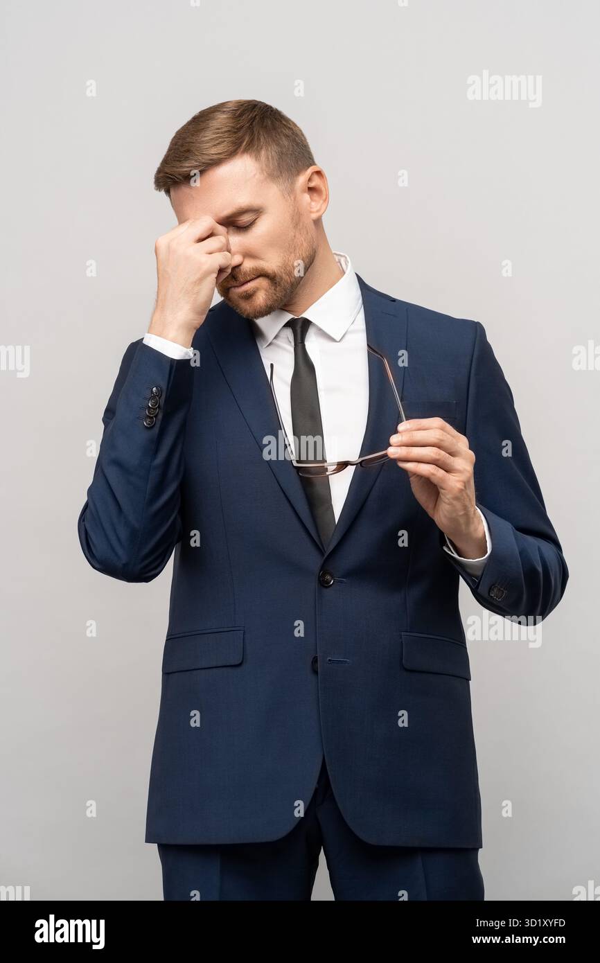 Frustrated businessman in emotional stress holds eyeglasses rubs bridge of nose on studio background Stock Photo