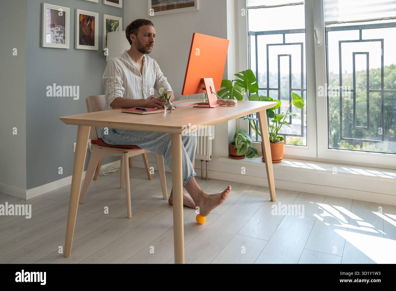 Man IT freelancer working on computer at home doing foot exercise using massage ball. Stock Photo