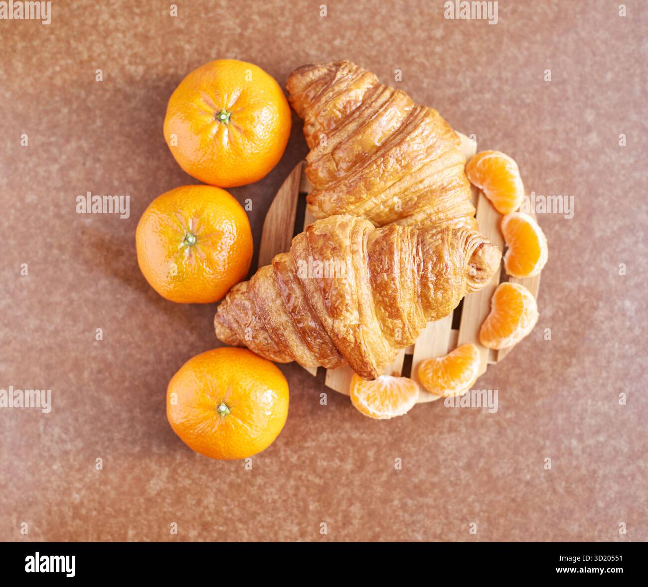 Delicious fresh croissants with vibrant oranges and sliced tangerines on wooden Stock Photo