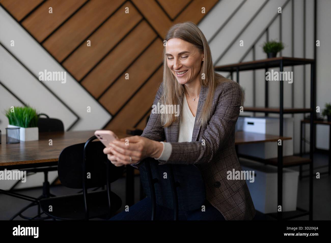 Professional woman smiling while using smartphone in modern office setting during daytime Stock Photo