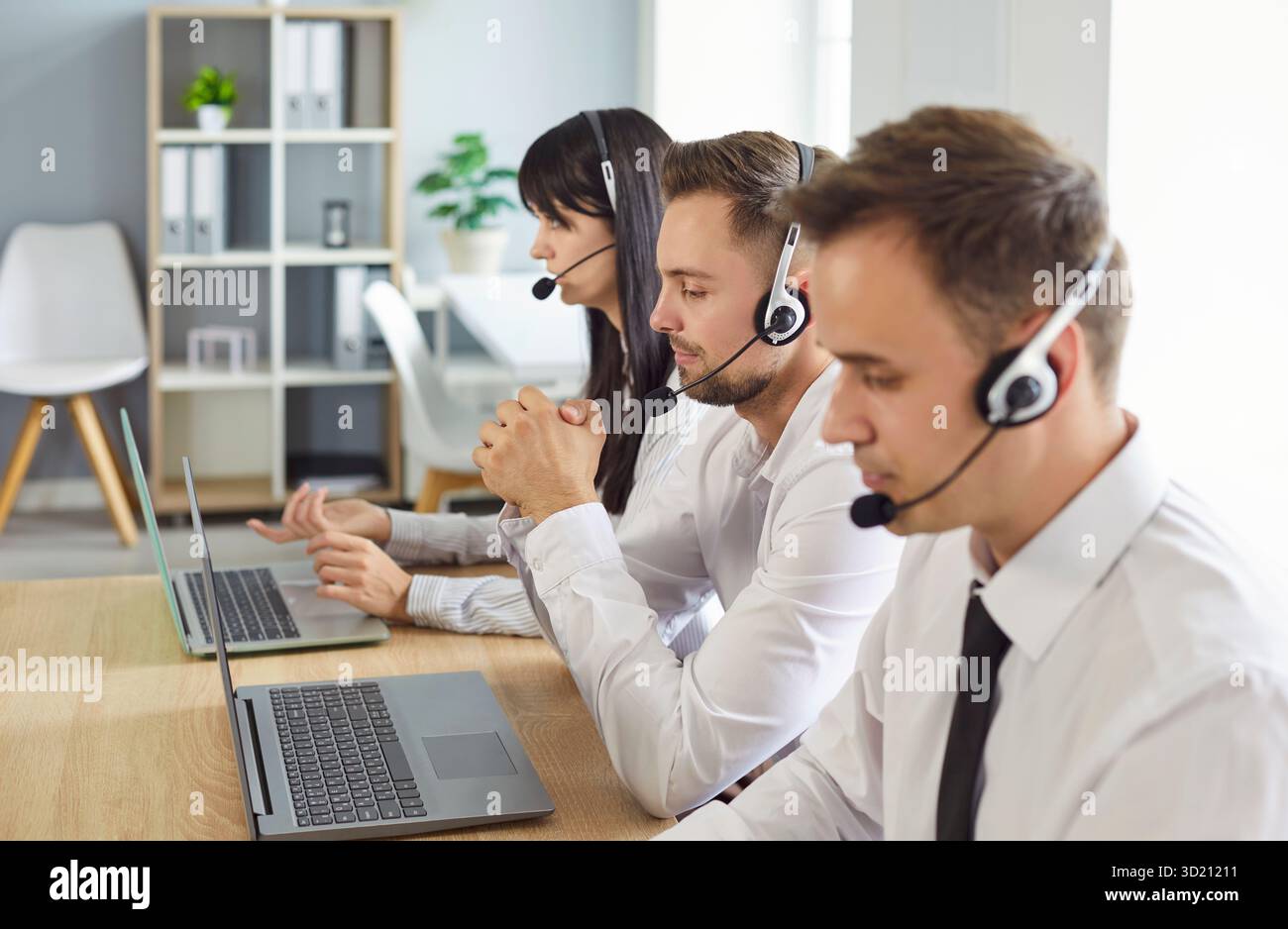 Focused support operators wearing headsets at desks with laptops in a office Stock Photo