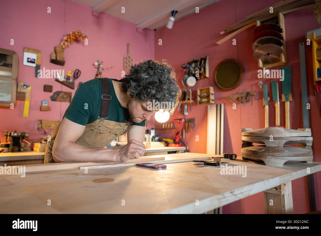 Focused woodworker carefully reviews client order specifications using smartphone in workshop Stock Photo