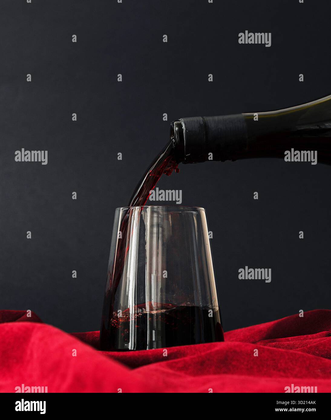 A hand pours a deep red wine from a bottle into a clear glass. The ...