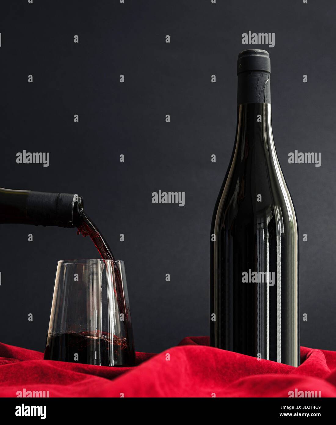 A hand pours rich red wine into a clear glass. A sleek bottle rests on ...