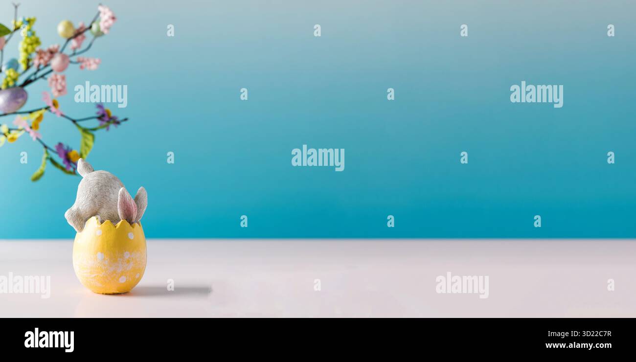 A white rabbit hid in an Easter egg on a blue background. Festive Easter card. Copy space. Stock Photo