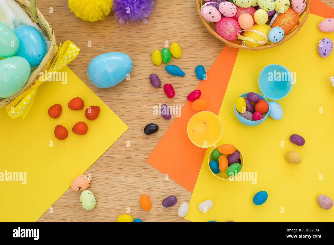 Bright background with candies in the form of Easter eggs in plastic eggs. Egg hunt concept. Happy Easter. Top view. Stock Photo
