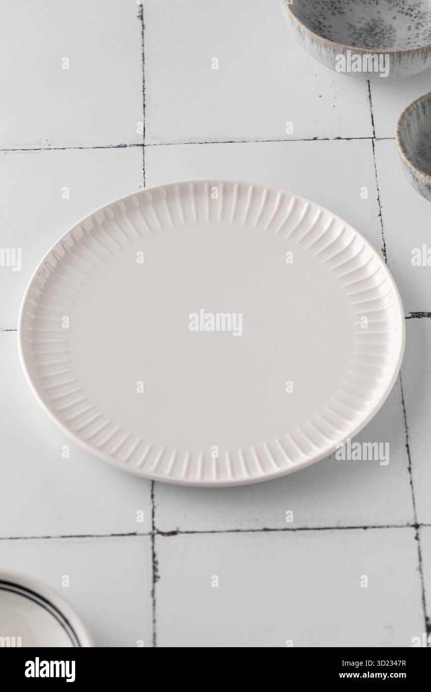 Minimalist white ceramic plate on a tiled surface. Kitchen, menu. Stock Photo