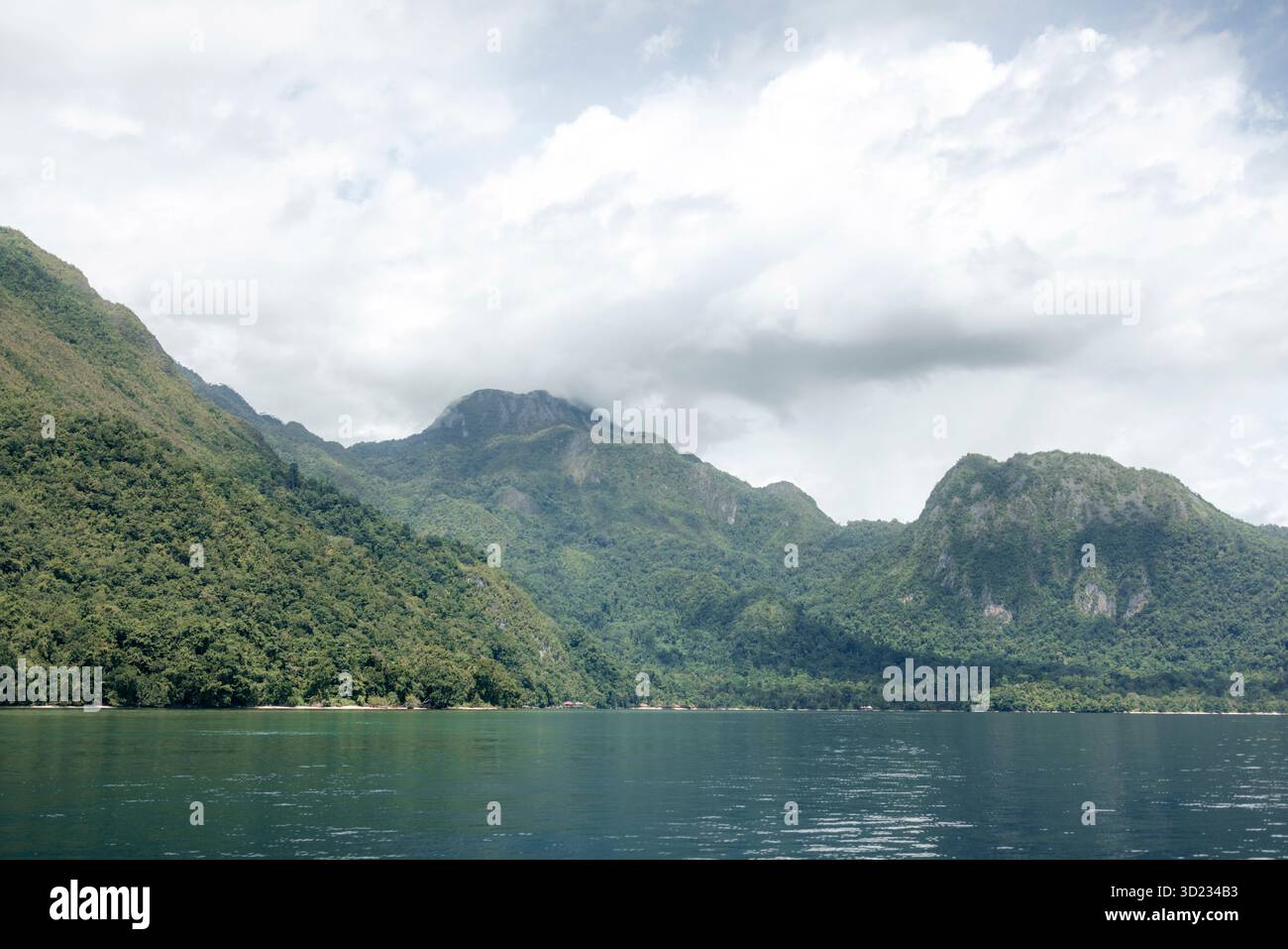 Lush green mountains and serene water under a cloudy sky in a tranquil landscape. Saleman Village, Seram Island, Maluku, Indonesia Stock Photo