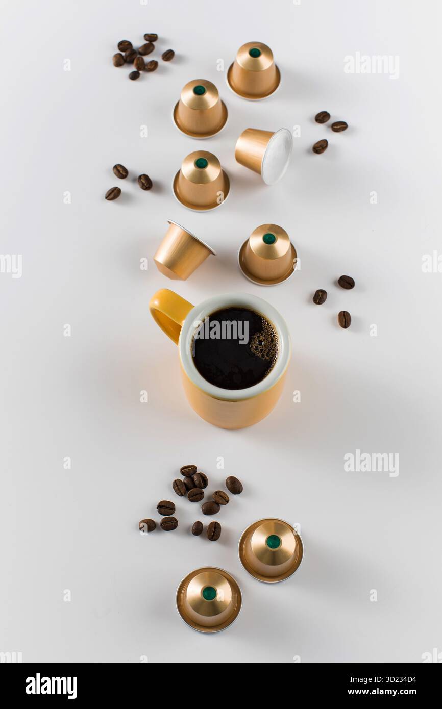 Yellow coffee cup with golden coffee capsules and beans on a white background. Stock Photo