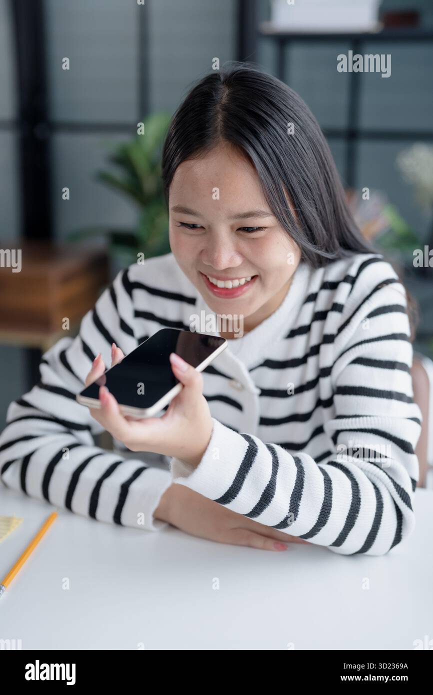 Asian Woman Engaging with Voice Assistant on Smartphone in Modern Home Stock Photo