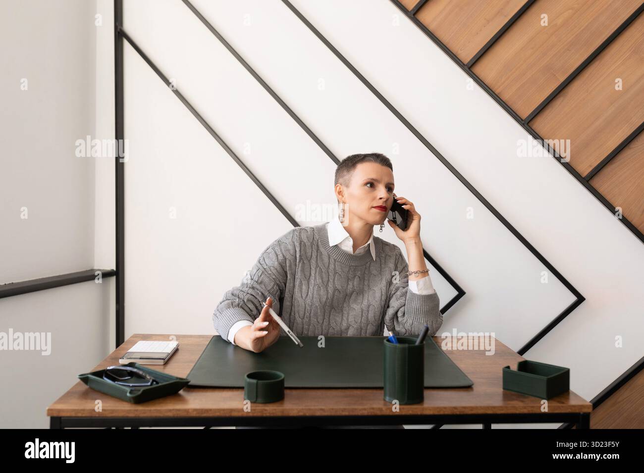 Business caucasian serious woman talking on mobile phone while sitting at table in office Stock Photo