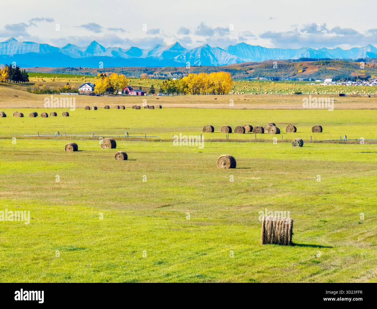 Rolling fields with hay bales and a backdrop of blue mountains under a ...