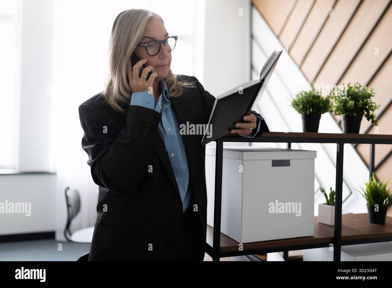 Middle aged older business woman in the office talking on a mobile phone Stock Photo
