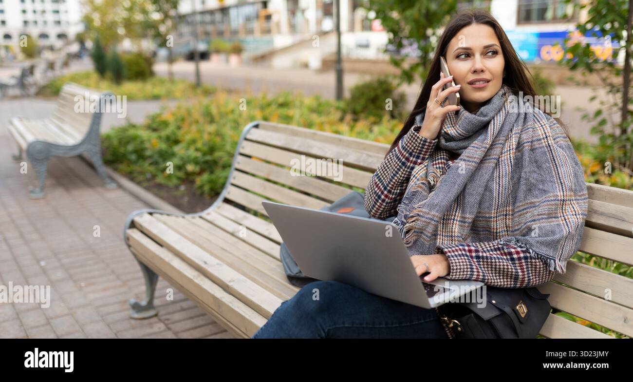 Female freelancer working online on laptop while sitting in city on wooden benches Stock Photo