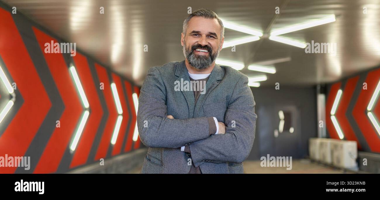 A gray-haired fifty-year-old man businessman in an underground parking lot stands with his arms folded across his chest Stock Photo