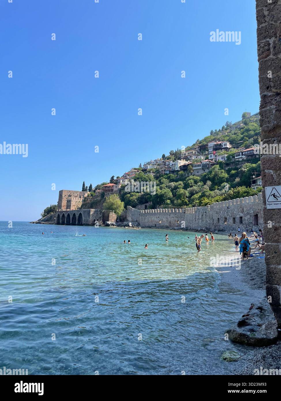 Historic seaside fortress and old houses on a green hillside above the Mediterranean Sea in sunny weather. Scenic coastal view with turquoise water. - Smartphone Captured Stock Image