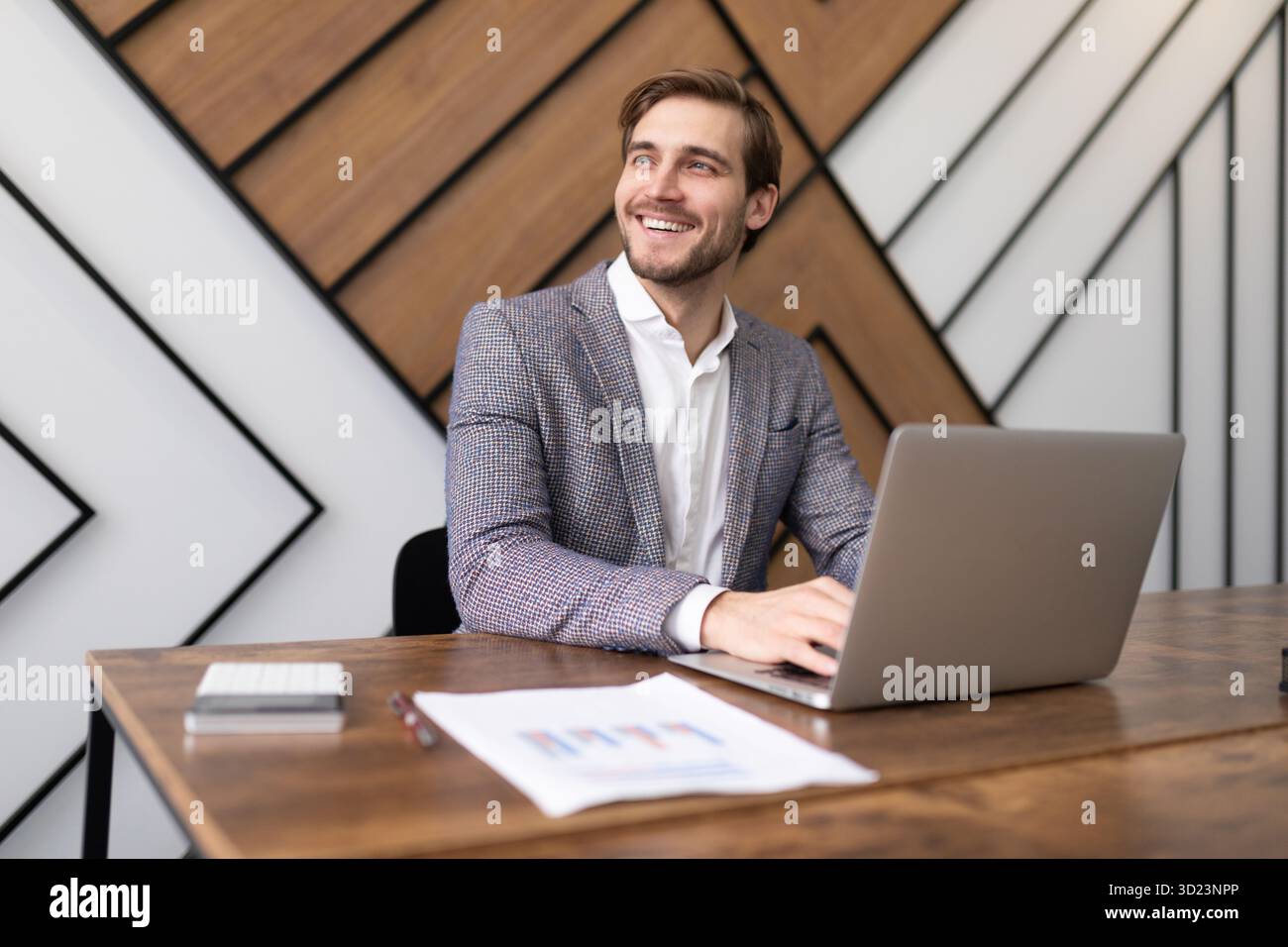 Smiling businessman working on laptop and looking out the window Stock Photo