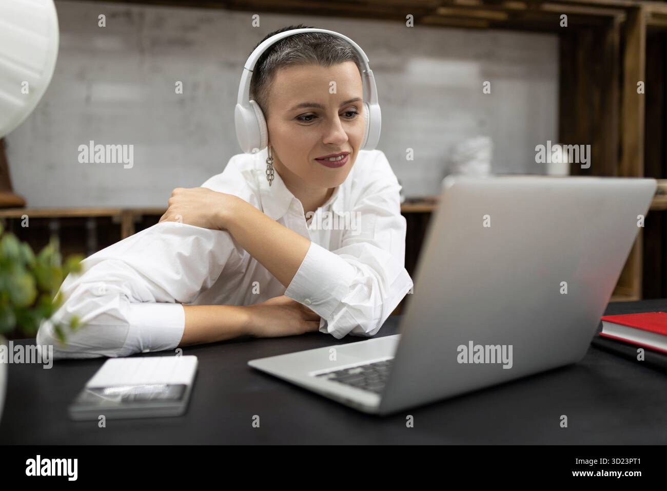 Business woman watching a webinar in headphones on a laptop while sitting at a table in the office Stock Photo
