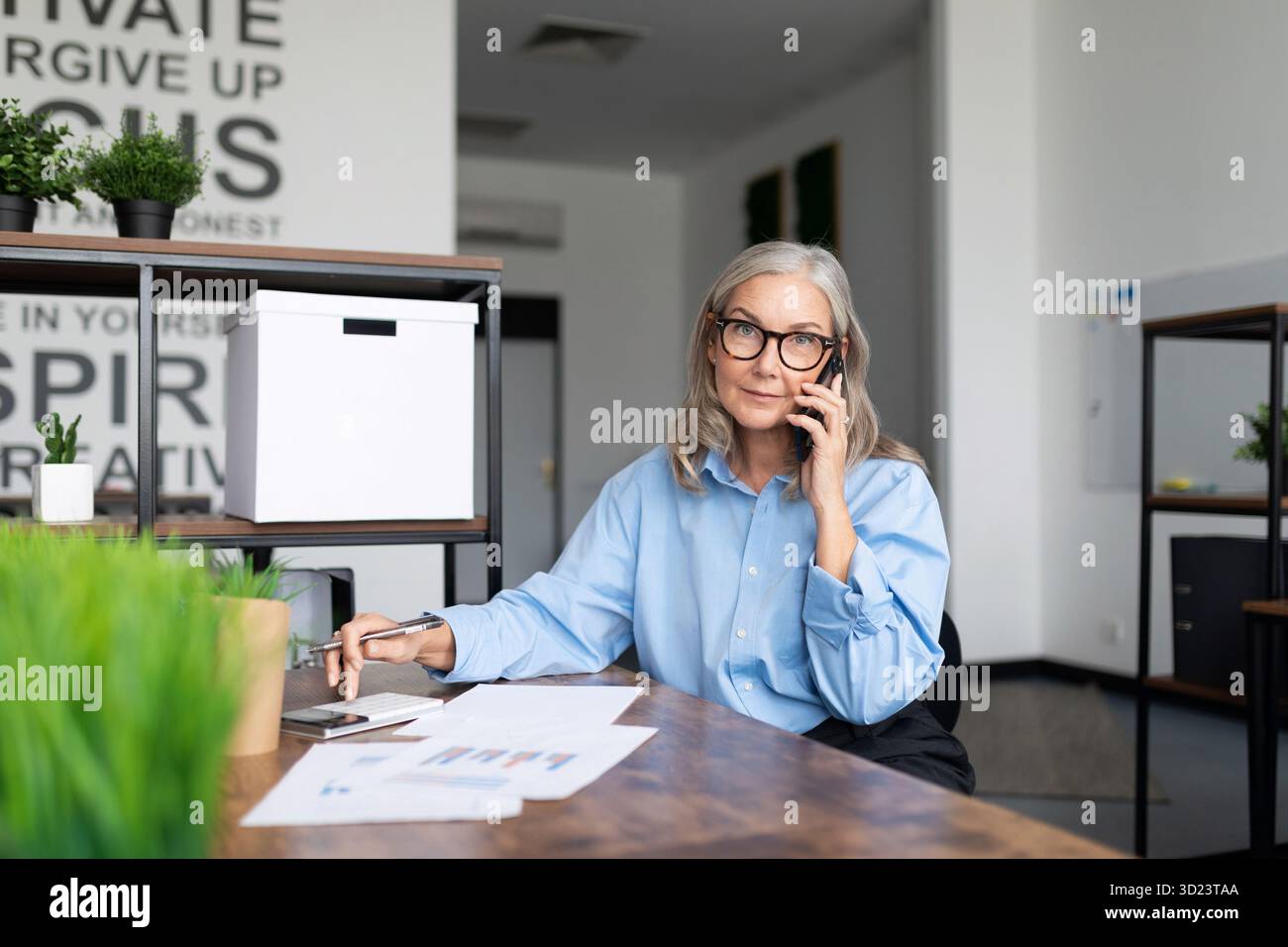 Business fifty year old female accountant prepares documents Sitting in the office talking on a mobile phone. Professional Accou Stock Photo
