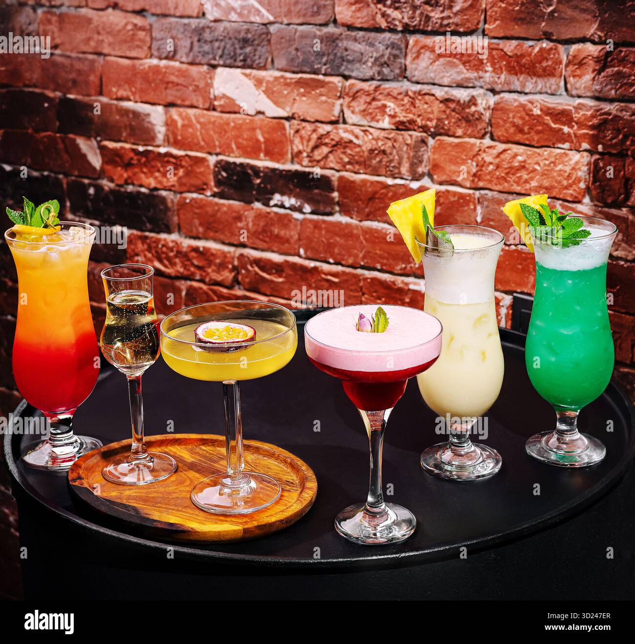 A variety of vibrant cocktails are displayed on a dark surface inside a ...