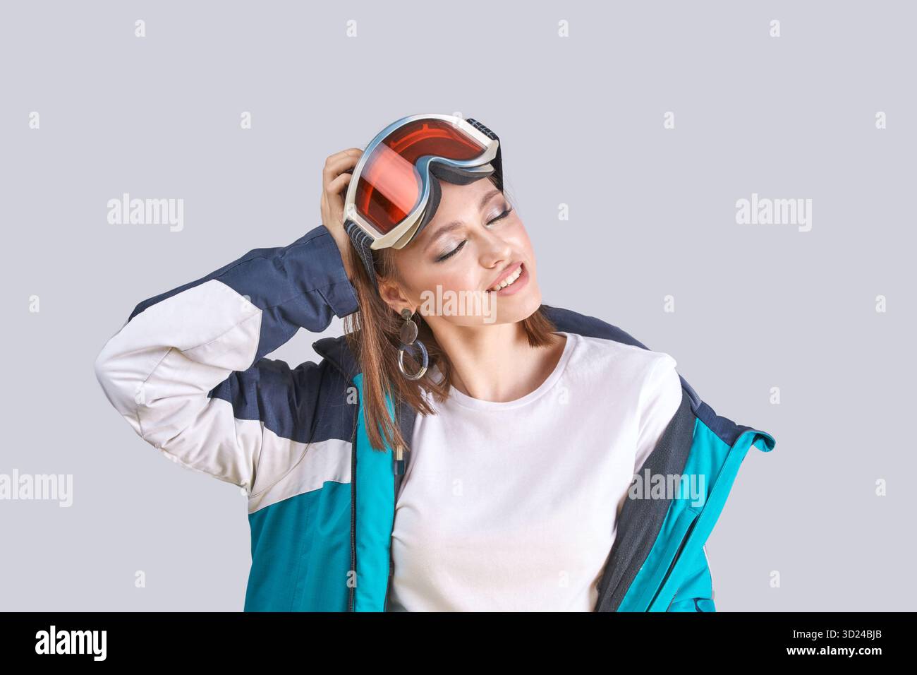 Young caucasian female wearing ski jacket and goggles in relaxed pose on gray Stock Photo