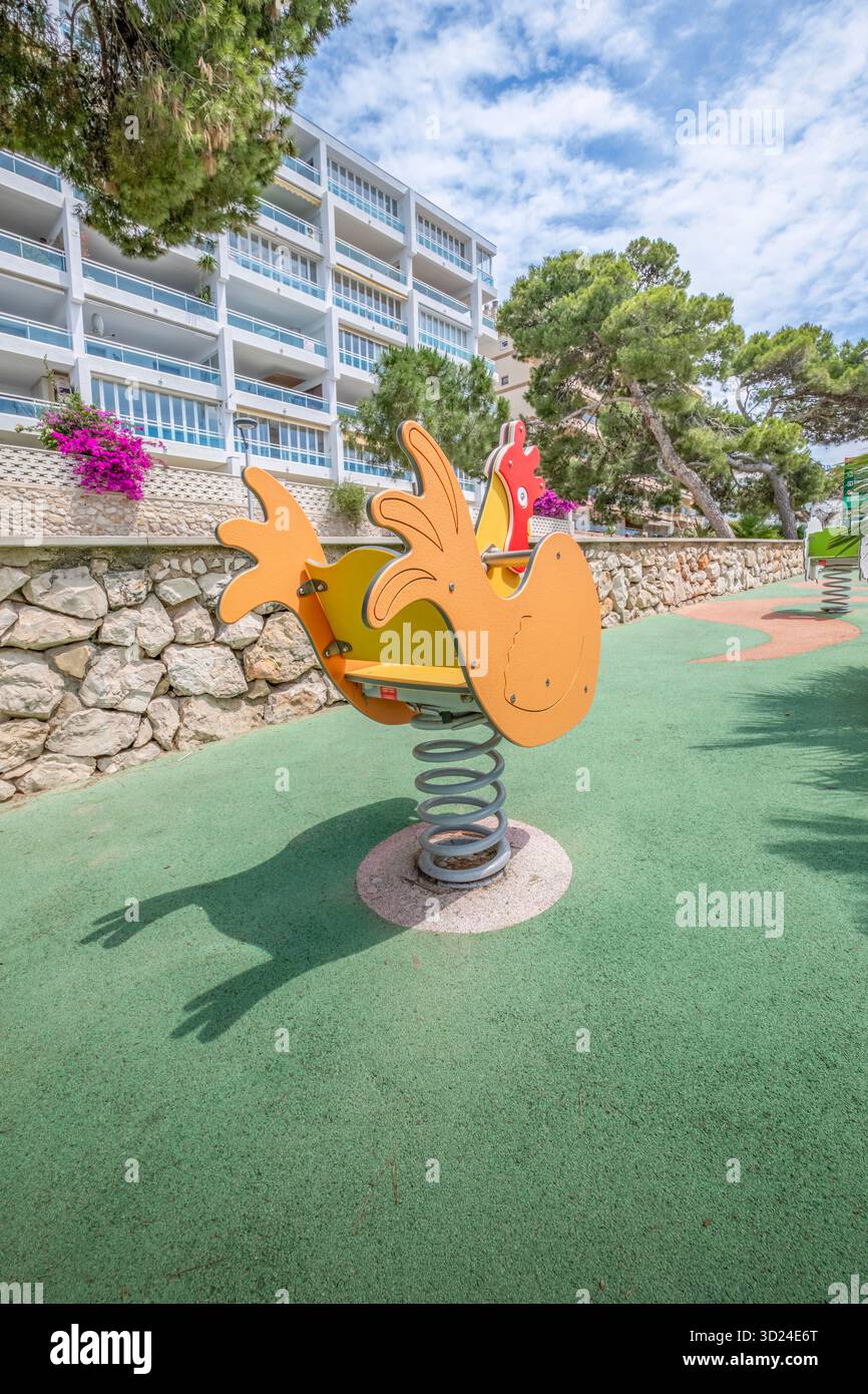 Empty orange rooster spring rider on a playground near a stone wall and ...