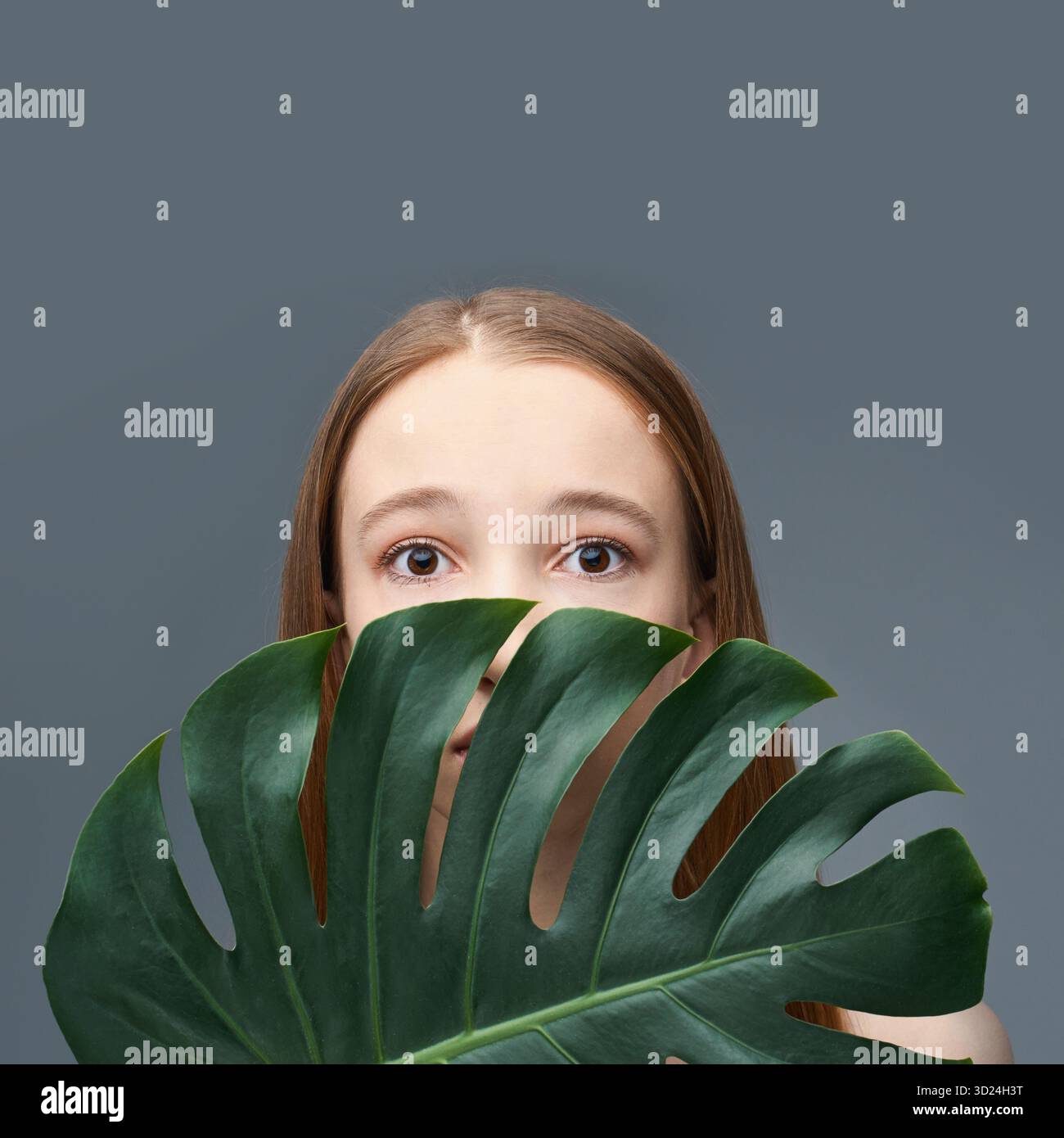 Young caucasian female with monstera leaf against gray background featuring Stock Photo