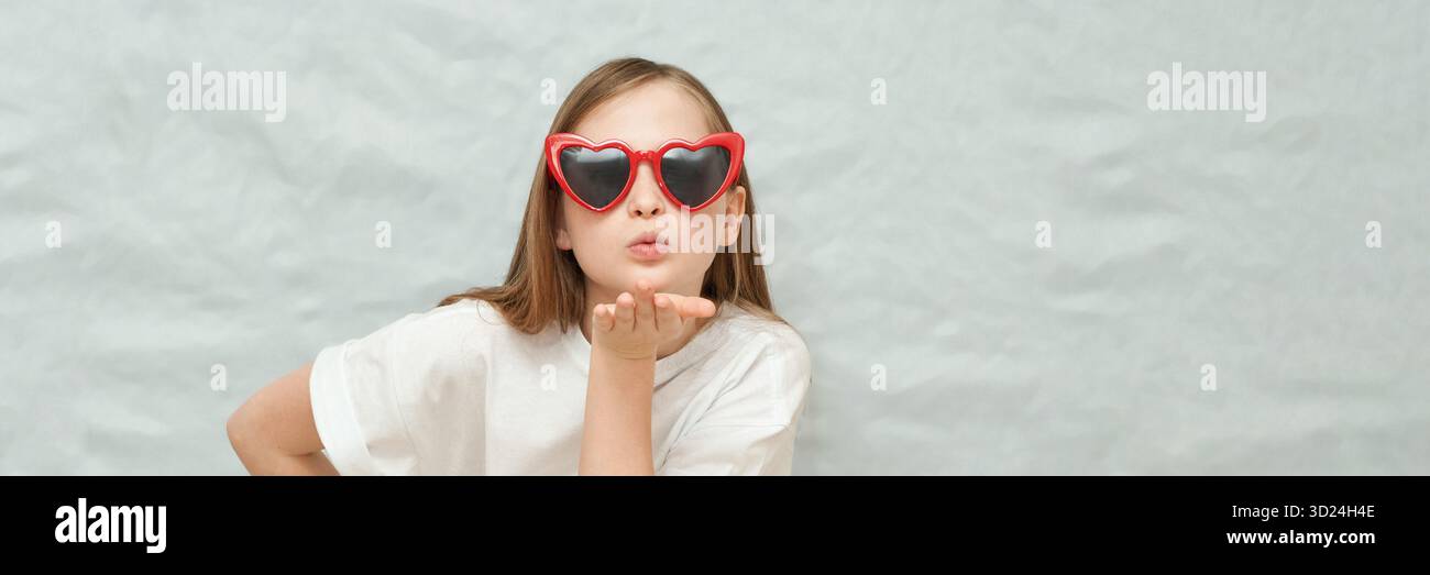 Caucasian young girl blowing kiss wearing red heart sunglasses against grey Stock Photo
