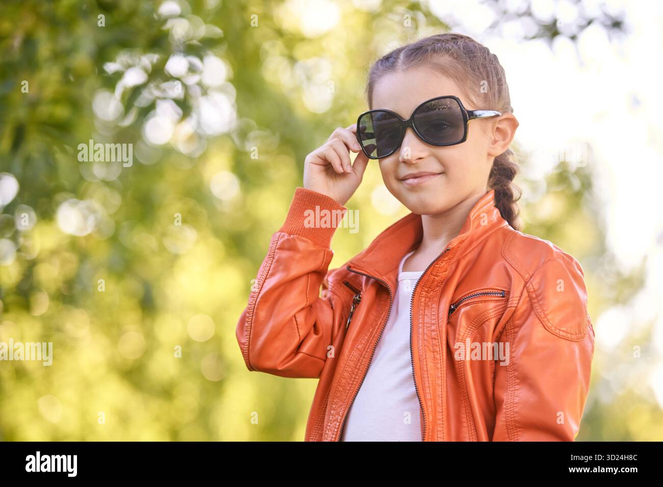 Young caucasian female child in orange jacket wearing sunglasses outdoors Stock Photo