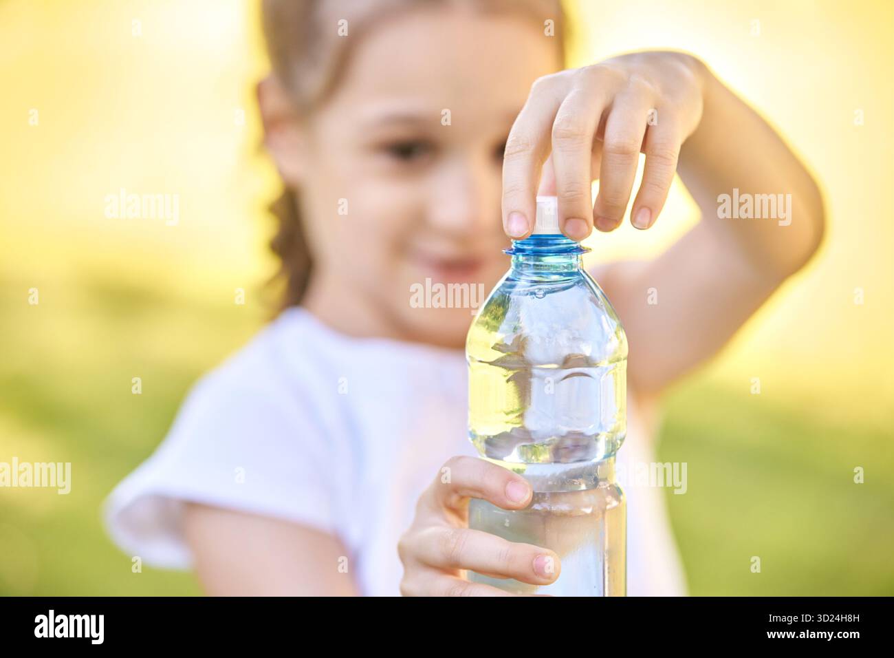 Hispanic female child opening water bottle in sunny outdoor setting with focus Stock Photo