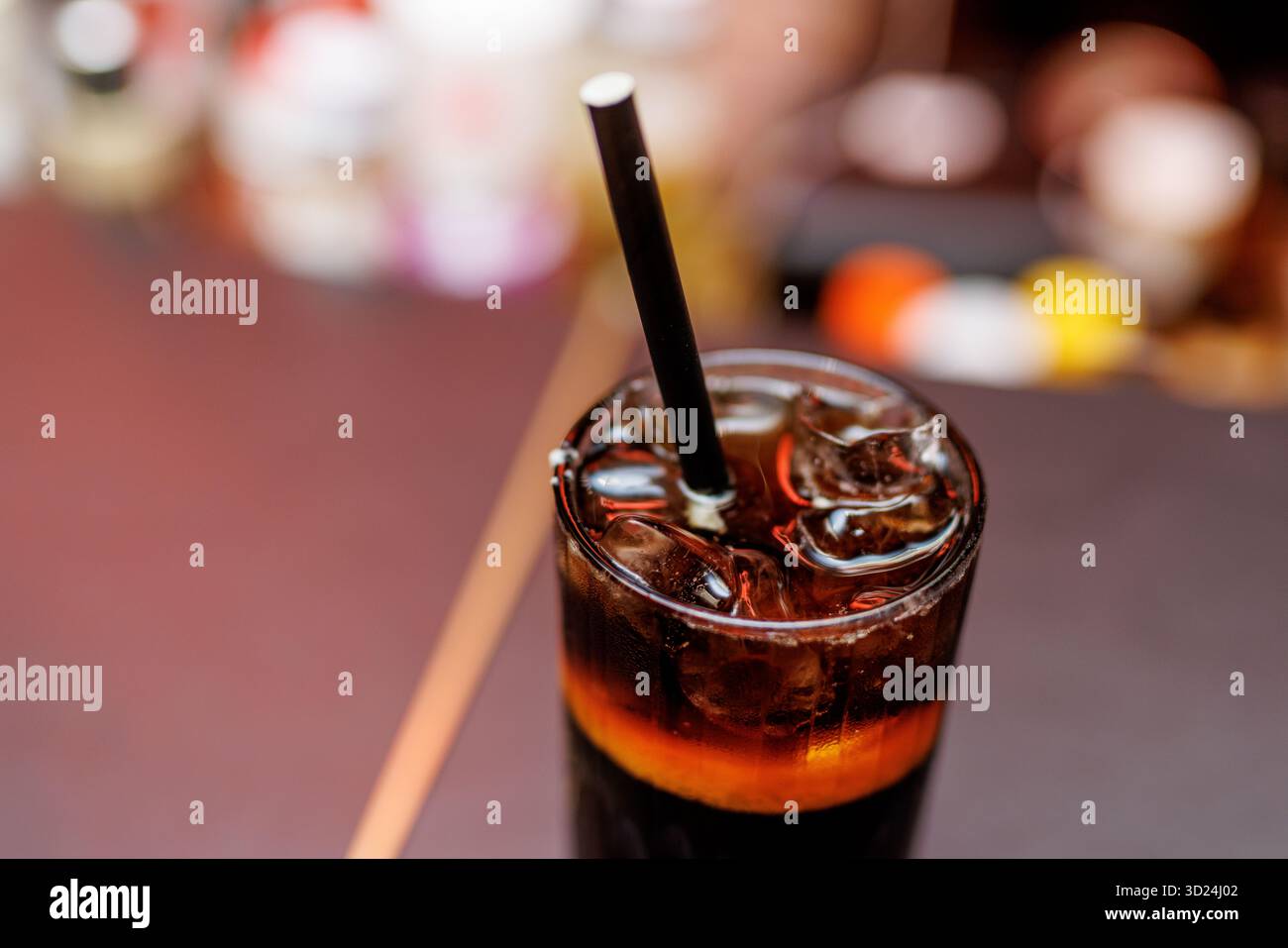 Chilled cola with ice cubes and a black straw served in a glass ...