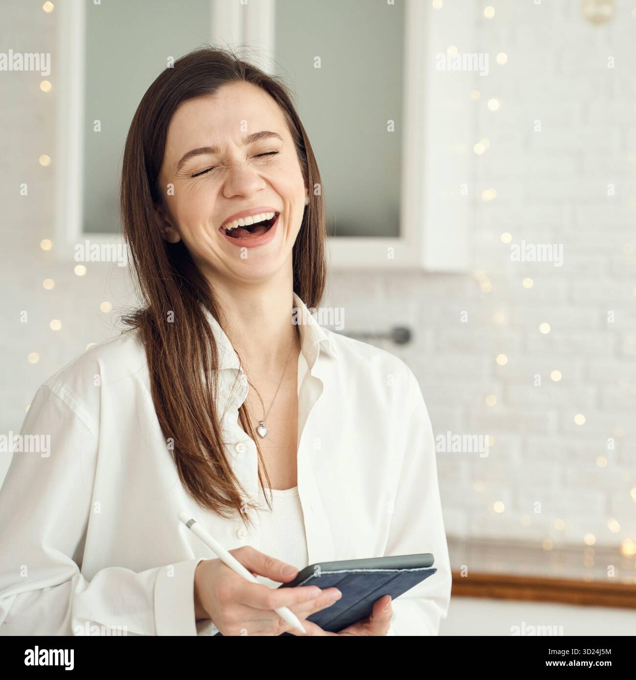 Young caucasian female laughing indoors holding tablet in bright room Stock Photo