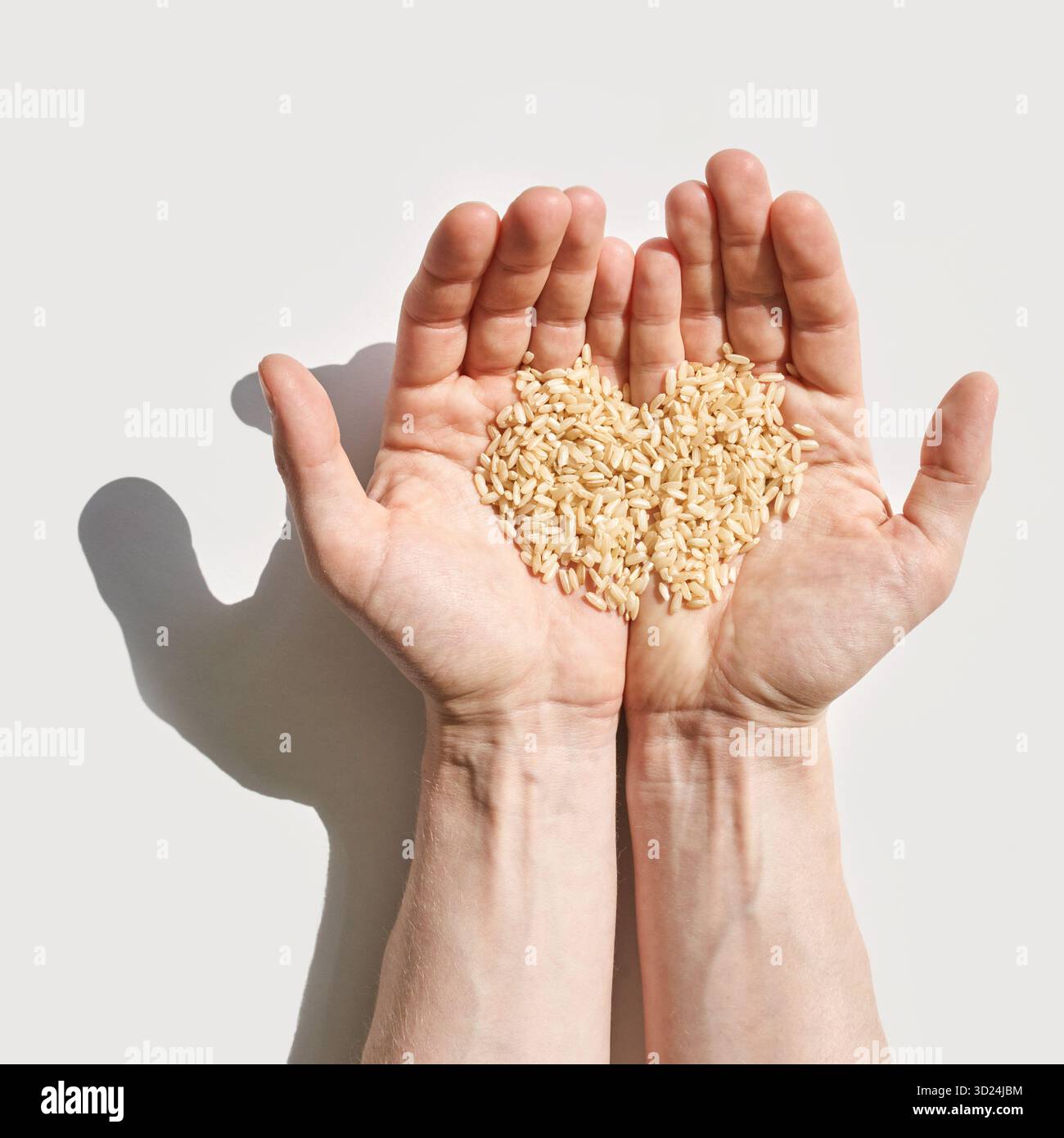 Caucasian adult hands holding heart-shaped rice grains on white background Stock Photo