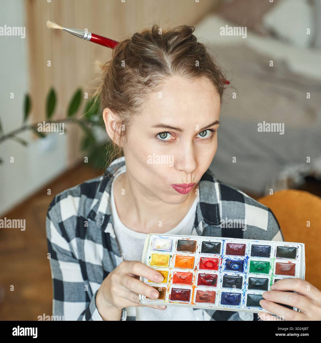Young caucasian female artist with watercolor palette and paintbrush hair Stock Photo