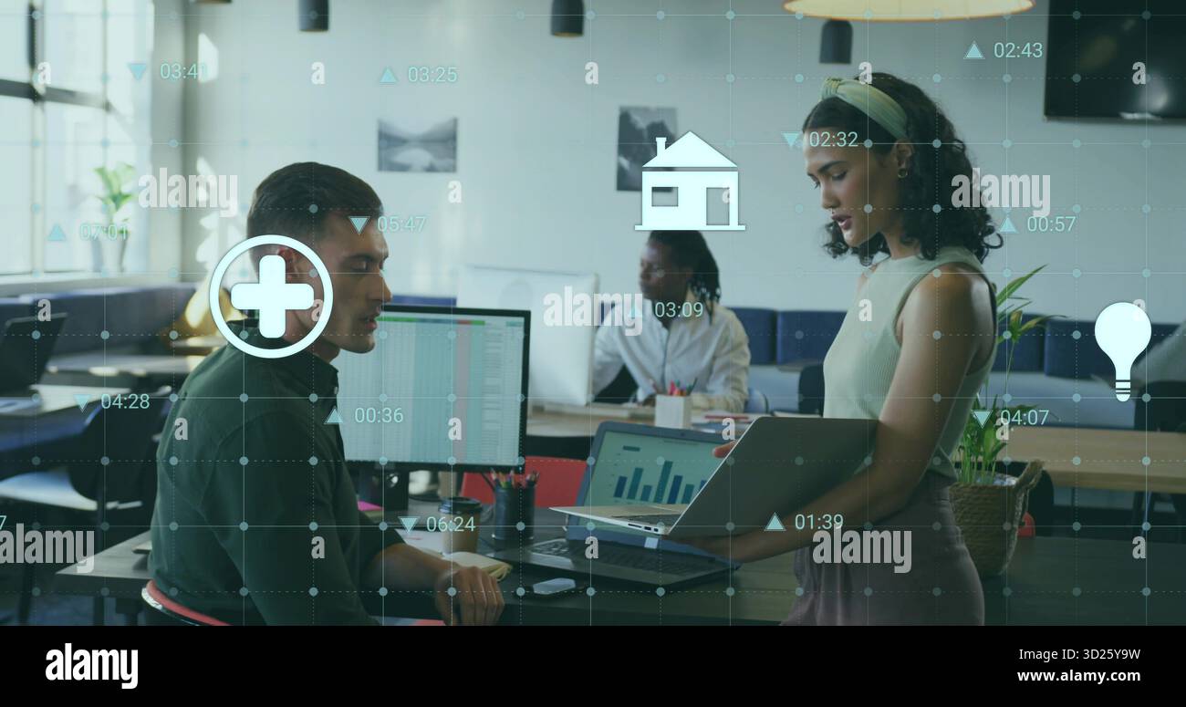 Holding laptop, office worker discussing data with coworker in open-plan office, digital icons Stock Photo