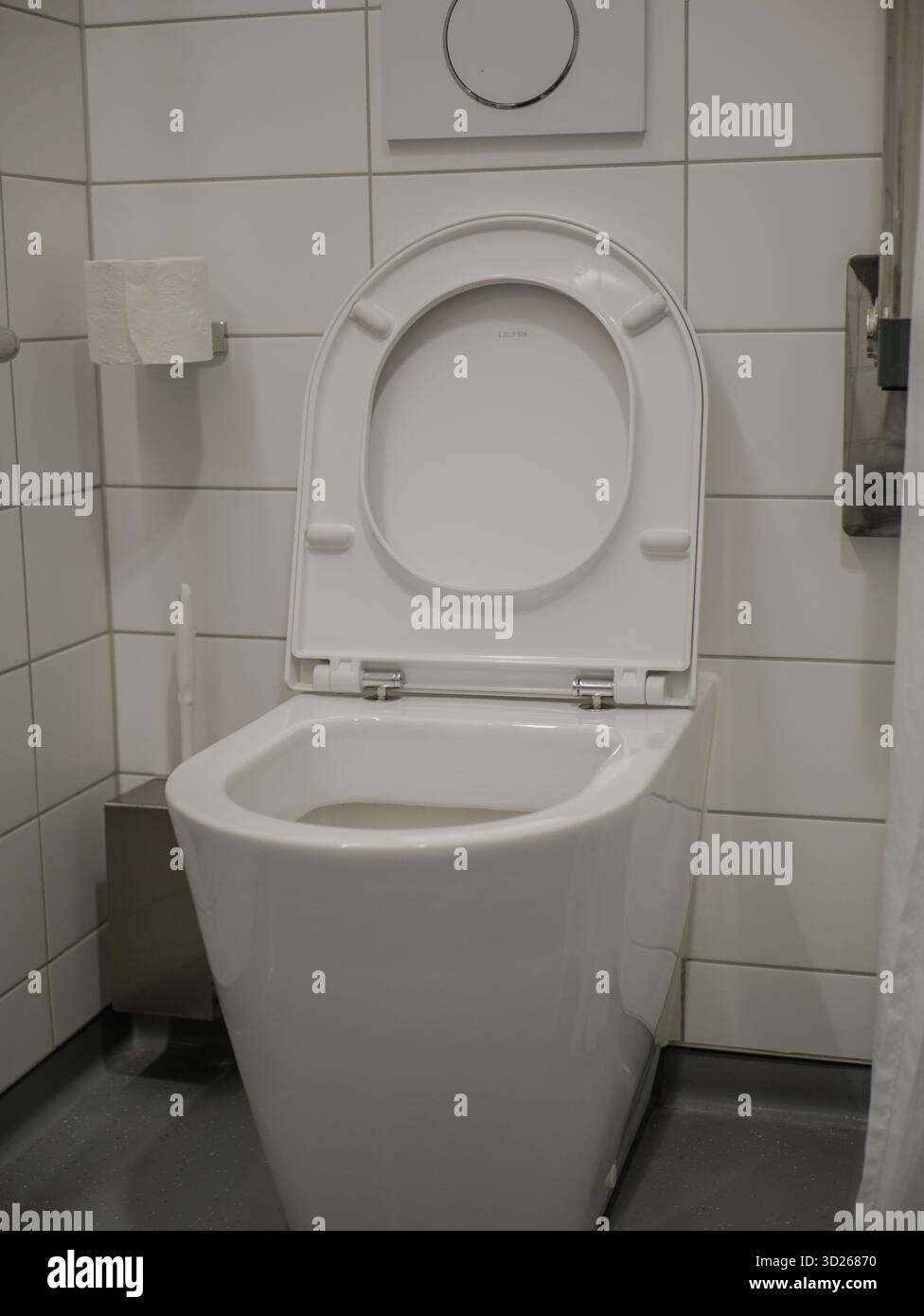 Clean modern white toilet in hospital bathroom with tiled walls,