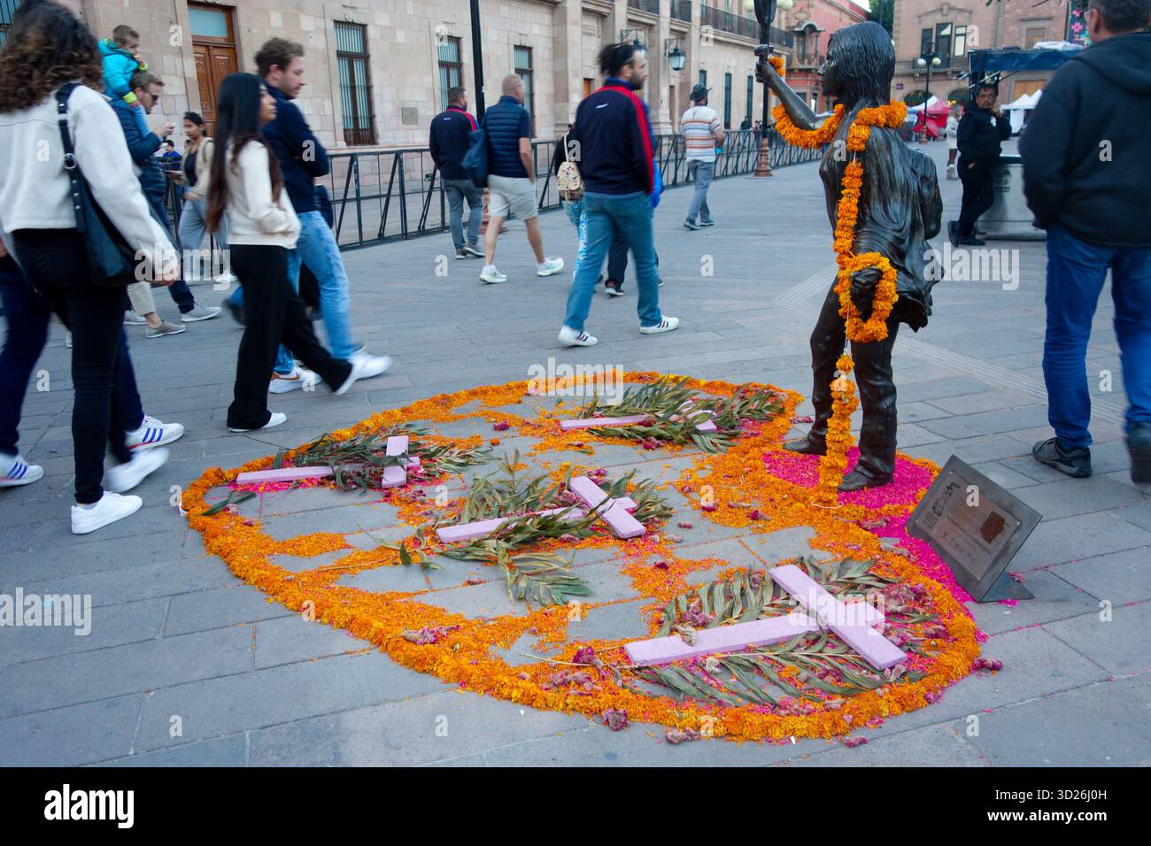 Pedestrians pass a street memorial with marigold flowers and crosses arranged around a statue during Day of the Dead in Centro,San Luis Potosi, Mexico Stock Photo
